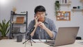 Young adult Asian businessman podcasting and recording online talk show at home studio using microphone and laptop, Attractive Royalty Free Stock Photo