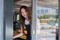 Young adult Asian female barista welcoming a customer walking into the coffee shop with a friendly smile and warm Royalty Free Stock Photo