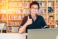 Young adult Asian man with laptop, thumbs up ok sign, home office or library scene, with copy space, success or technology concept Royalty Free Stock Photo