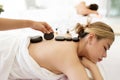 Young adult Asian woman lying down and getting hot basalt stone massage on her back by masseur or therapist in spa salon. Royalty Free Stock Photo