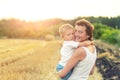 Young adult attractive beautiful mom holding on hand and hugging little son enjoy walking by golden wheat harvested field near Royalty Free Stock Photo