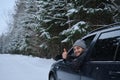 Young adult attractive Caucasian man sits at the wheel of his car snowy winter day showing thumbs up gesture. Wintertime