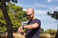 Young adult,bald and bearded wearing black sunglasses standing in nature on hot day checking his watch Royalty Free Stock Photo