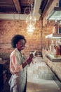 Young-adult beaming bewitching Afro-American bar employee holding towels at bar