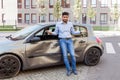 Young adult bearded man with sad expression standing with raised arms and looking at camera, being confused after car accident, Royalty Free Stock Photo