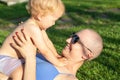 Young adult beautiful bald caucasian mom enjoy lying with little blond toddler boy son on green grass lawn at city park at summer Royalty Free Stock Photo