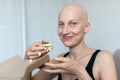 Young adult beautiful caucasian bald shaved hair woman portrait enjoy eating sandwich for lunch at home indoor. Breast cancer