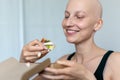 Young adult beautiful caucasian bald shaved hair woman portrait enjoy eating sandwich for lunch at home indoor. Breast cancer Royalty Free Stock Photo