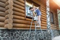 Young adult beautiful slim sporty caucasian woman in overalls stand on metal ladder and washing window wooden house Royalty Free Stock Photo