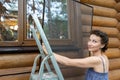 Young adult beautiful slim sporty caucasian woman stand on metal ladder and installing window mosquito insect fly screen