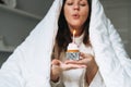 Young adult happy beautiful woman forty years plus size body positive in white blanket with festive cupcake with candle in hands Royalty Free Stock Photo