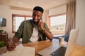 Young adult black African American male smiling while on a phone call. Writing in his notepad, working from laptop at