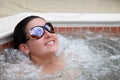 Young adult woman brunette lounging in hot tub with sunglasses smiling with bubbles Royalty Free Stock Photo