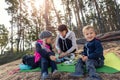 Young adult caucasian beautiful mother enjoy having fun eating snack on picnic with two cute little children in pine forest