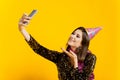 A young adult cheerful girl 20-25s in a festive hat and New Year`s tinsel takes a selfie or films herself on a smartphone Royalty Free Stock Photo
