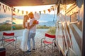 young adult couple hugging, holding each other in arms, in love, in front of a camper outdoor at the sunset and beautiful view Royalty Free Stock Photo