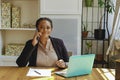 Young adult entrepreneur freelance black woman small business owner with laptop talking on mobile phone smiling in home Royalty Free Stock Photo