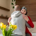 Young adult female cancer patient hugging her husband at home after treatment in hospital. Cancer and family support. Royalty Free Stock Photo