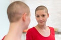 Young adult female cancer patient looking in the mirror, smiling.