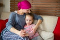 Young adult female cancer patient spending time with her daughter at home, relaxing on couch. Cancer and family support concept.