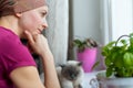 Young adult female cancer patient wearing headscarf and bathrobe sitting in the kitchen with her pet cat.