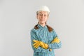 A young adult female construction worker in a white construction helmet stands with her arms crossed on a gray background Royalty Free Stock Photo