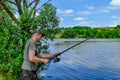 Young adult fisherman casts a fishing rod into the river. Portrait of a man fishing on a background of beautiful juicy green Royalty Free Stock Photo