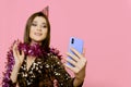 A young adult girl 20-25s in a festive hat and New Year`s tinsel takes a selfie or shoots a video on a smartphone Royalty Free Stock Photo