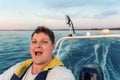 Young adult happy caucasian excited man portrait enjoy having fun driving fast motorboat on pond water surface at sunset