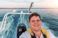 Young adult happy caucasian excited man portrait enjoy having fun driving fast motorboat on pond water surface at sunset