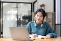 Young adult happy smiling Asian student wearing headphones talking on online chat meeting using laptop in university Royalty Free Stock Photo