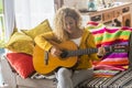 Young adult happy woman singing an acoustic guitar smiling at home, Concept of playing song and having fun alone. Learning music