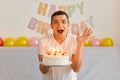 Young adult joyful excited man holding a birthday cake and looking at the camera with open mouth, yelling happily, wearing white t Royalty Free Stock Photo