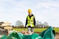 A young adult male builder wearing a high visibility vest and hard hat pushing a wheelbarrow full of bricks while on a building Royalty Free Stock Photo