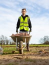 A young adult male builder wearing a high visibility vest and hard hat pushing a wheelbarrow full of bricks while on a building Royalty Free Stock Photo