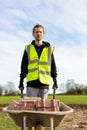 A young adult male builder wearing a high visibility vest and hard hat pushing a wheelbarrow full of bricks while on a building Royalty Free Stock Photo