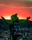 Young adult male on a motorbike, arms outstretched in a triumphant gesture at sunset