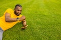 Young adult male sitting on the grass in stylish sportswear after workout, hold a smartphone, relaxing. Sportive african