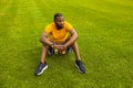 Young adult male sitting on the grass in stylish sportswear after workout, hold a smartphone, relaxing. Sportive african