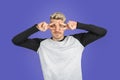 Young adult man on casual clothing gesturing with peace or v sign between his eyes. Isolated studio shot on purple background