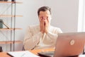 A young adult man in a home office working on a laptop is tired and covers his eyes with his hands Royalty Free Stock Photo