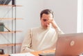 A young adult man in a home office working on a laptop is tired and covers his eyes with his hand Royalty Free Stock Photo