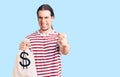 Young adult man with long hair holding money bag with dollar symbol annoyed and frustrated shouting with anger, yelling crazy with Royalty Free Stock Photo