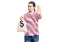 Young adult man with long hair holding money bag with dollar symbol with open hand doing stop sign with serious and confident Royalty Free Stock Photo