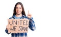 Young adult man with long hair holding united we stand banner surprised with an idea or question pointing finger with happy face,