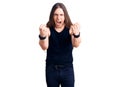 Young adult man with long hair wearing goth style with black clothes angry and mad raising fists frustrated and furious while
