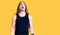 Young adult man with long hair wearing goth style with black clothes angry and mad screaming frustrated and furious, shouting with
