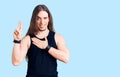Young adult man with long hair wearing goth style with black clothes smiling swearing with hand on chest and fingers up, making a