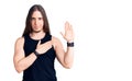 Young adult man with long hair wearing goth style with black clothes swearing with hand on chest and open palm, making a loyalty