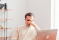 A young adult man in an office working on a laptop is tired and covers his eyes with his hand Royalty Free Stock Photo